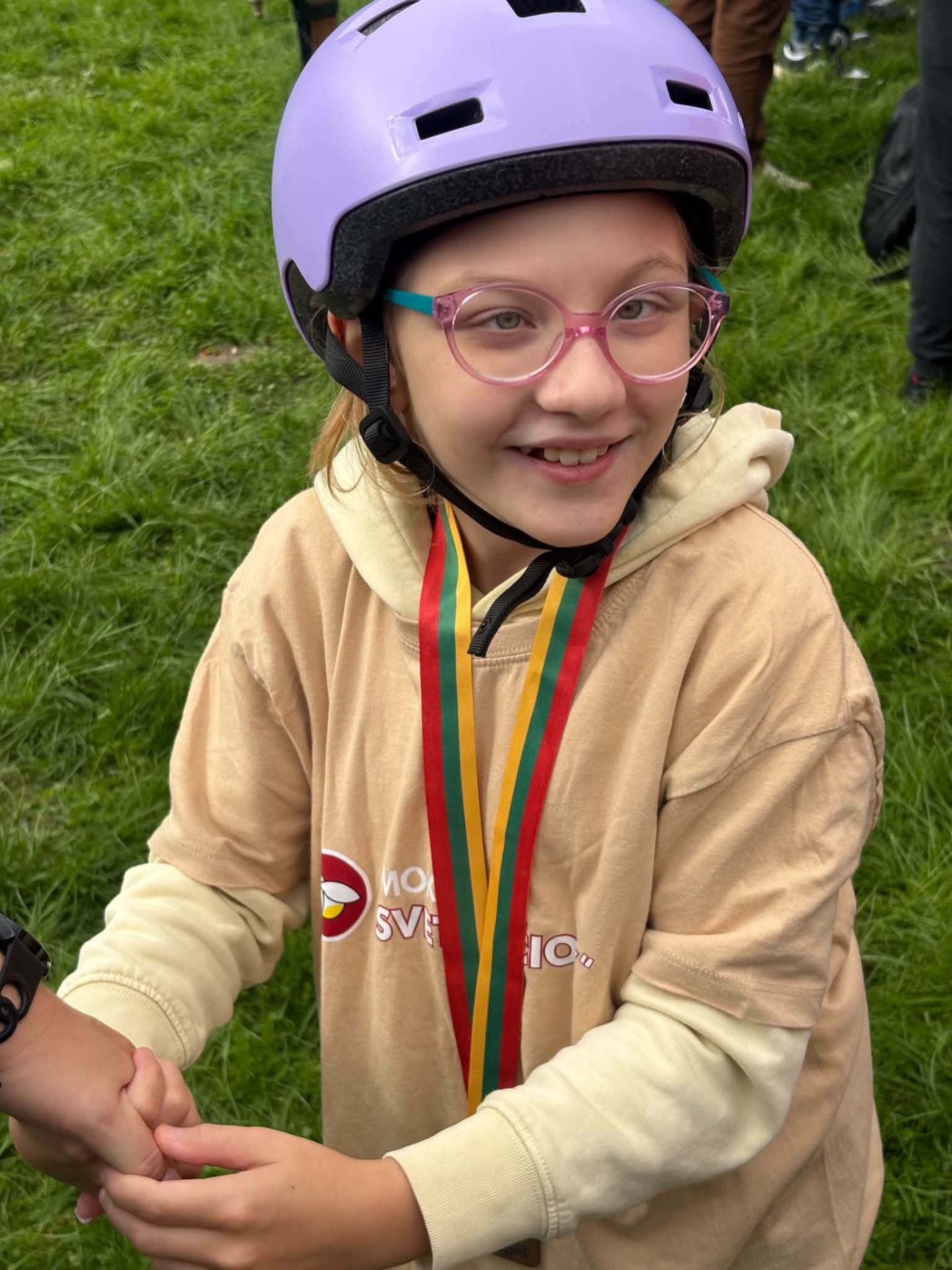Besišypsanti Aistė su šalmu ir medaliu lauke
